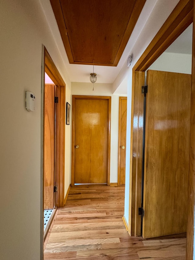 corridor featuring baseboards, attic access, and light wood-type flooring