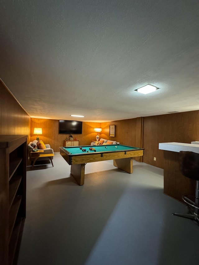 recreation room featuring pool table, a textured ceiling, wood walls, and concrete floors