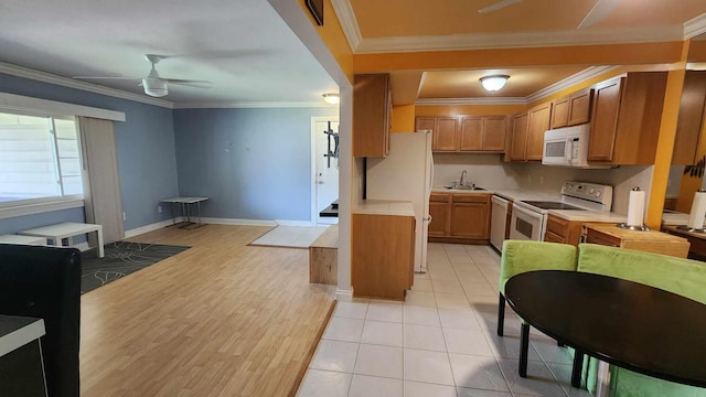kitchen with a sink, white appliances, brown cabinetry, crown molding, and light countertops