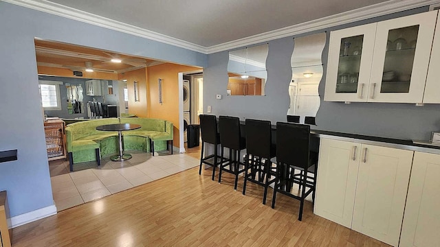 kitchen featuring stacked washer / drying machine, light wood-type flooring, crown molding, white cabinetry, and dark countertops