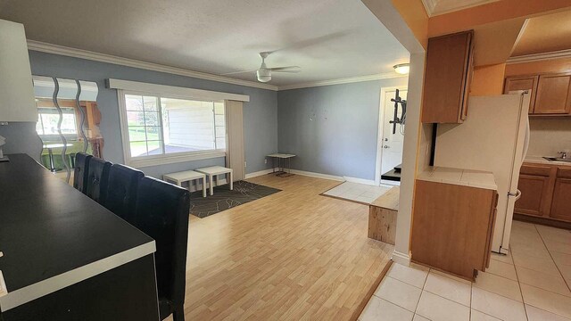 kitchen with brown cabinets, a ceiling fan, freestanding refrigerator, and crown molding
