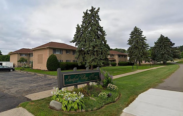 community / neighborhood sign with uncovered parking and a lawn