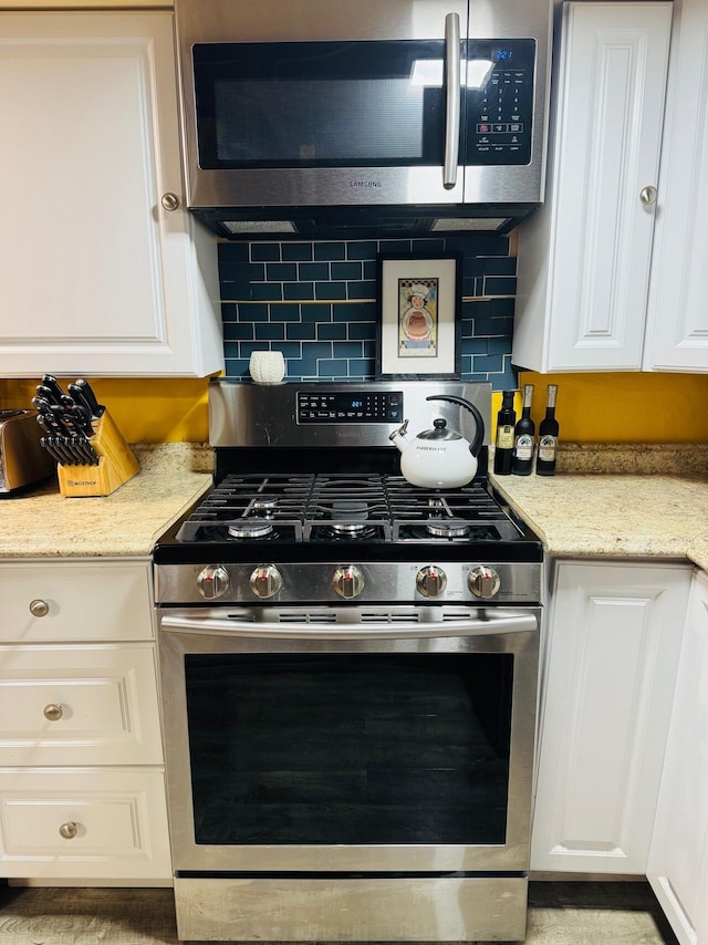 1106 Houghton View Dr, Houghton Lake, MI 48629 - kitchen with stainless steel appliances, white cabinetry, backsplash, and light stone counters