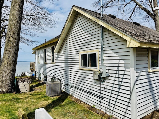 1106 Houghton View Dr, Houghton Lake, MI 48629 - view of property exterior with central AC, a lawn, a water view, and a shingled roof
