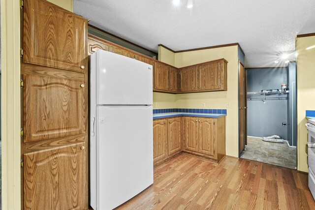 kitchen featuring brown cabinetry, freestanding refrigerator, light wood finished floors, and a textured ceiling