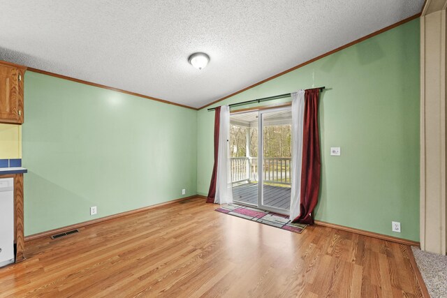 spare room with visible vents, ornamental molding, light wood-style flooring, and vaulted ceiling