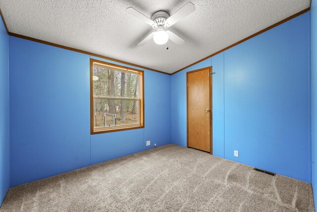 carpeted empty room featuring ceiling fan, ornamental molding, lofted ceiling, and visible vents