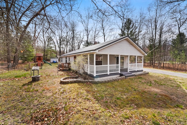 view of front of property featuring a front lawn, a playground, covered porch, and metal roof