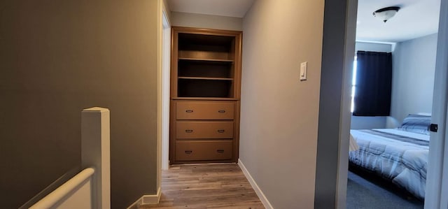 hallway featuring baseboards, built in shelves, and light wood finished floors