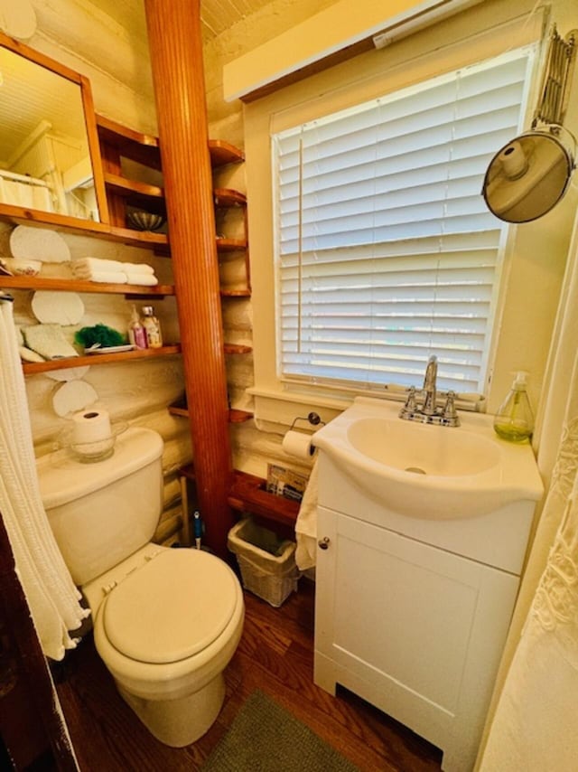 bathroom with rustic walls, toilet, wood finished floors, and vanity