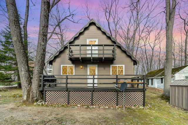 back of house at dusk featuring a wooden deck and a balcony