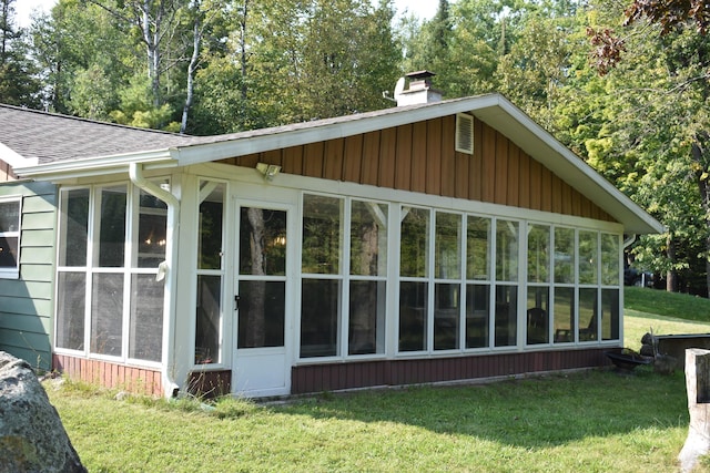 view of side of property featuring a sunroom, a yard, a shingled roof, and a chimney