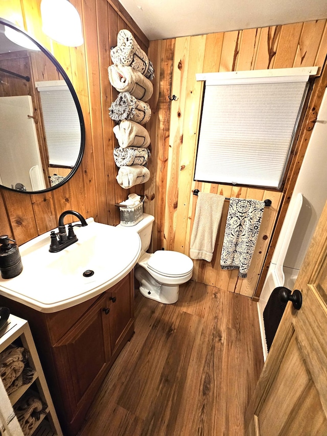 half bath featuring wood walls, wood finished floors, toilet, and vanity