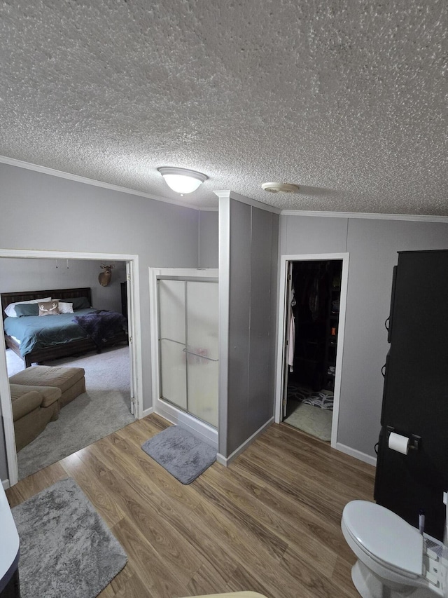 bathroom featuring a stall shower, ornamental molding, a textured ceiling, wood finished floors, and ensuite bathroom