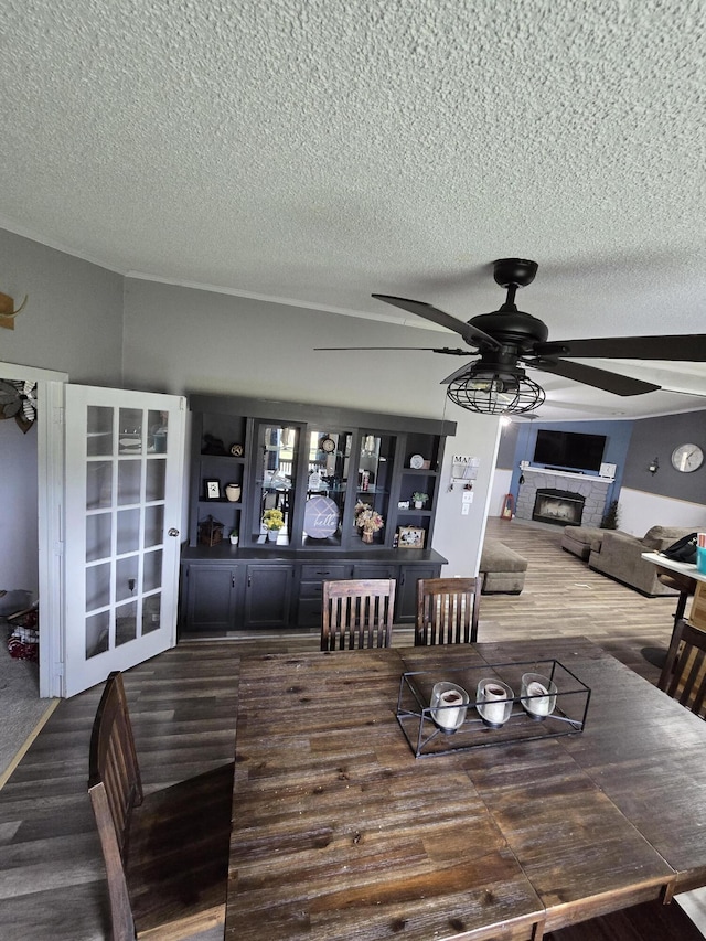 dining space with wood finished floors, a ceiling fan, a textured ceiling, and a glass covered fireplace