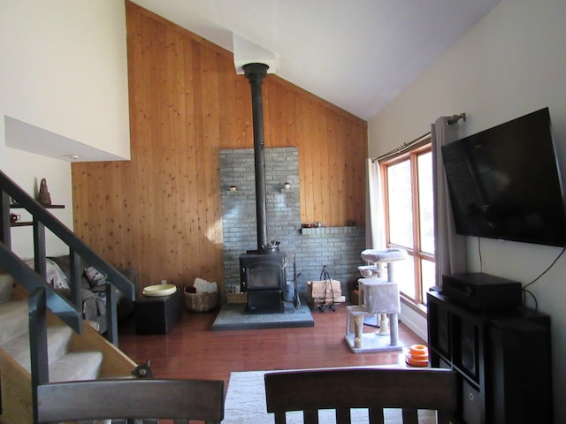 living room featuring a wood stove, wood walls, wood finished floors, stairway, and high vaulted ceiling