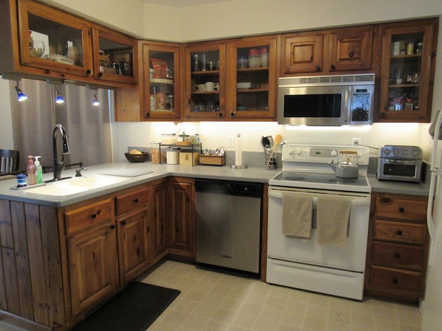 kitchen featuring a toaster, glass insert cabinets, light countertops, a sink, and stainless steel appliances
