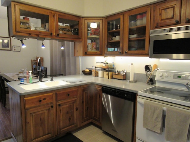 kitchen featuring light countertops, appliances with stainless steel finishes, brown cabinets, and glass insert cabinets