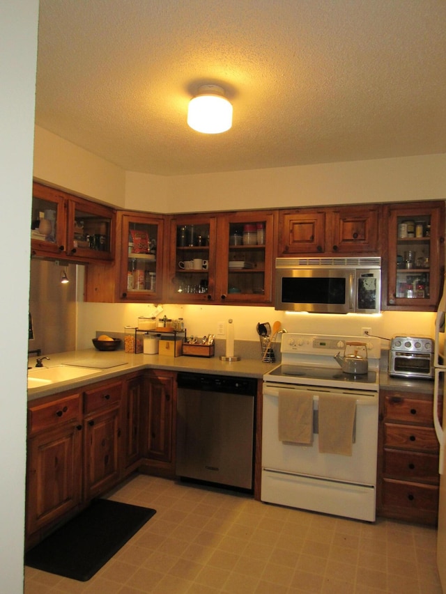 kitchen with light countertops, a textured ceiling, stainless steel appliances, a toaster, and glass insert cabinets