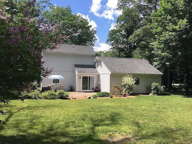 rear view of house featuring a yard, a patio, and roof with shingles