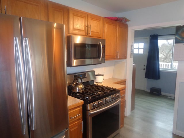 kitchen with appliances with stainless steel finishes, brown cabinets, light countertops, and light wood-style flooring