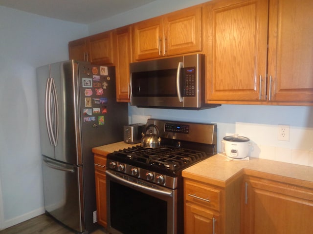 kitchen with baseboards, appliances with stainless steel finishes, brown cabinetry, and light countertops