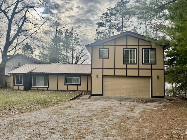view of front facade with a garage, dirt driveway, stucco siding, and metal roof