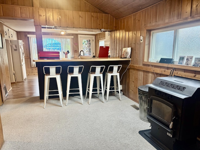 kitchen featuring wood walls, freestanding refrigerator, a peninsula, lofted ceiling, and a wood stove