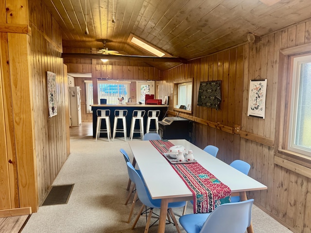 dining area with visible vents, wood walls, carpet floors, and lofted ceiling