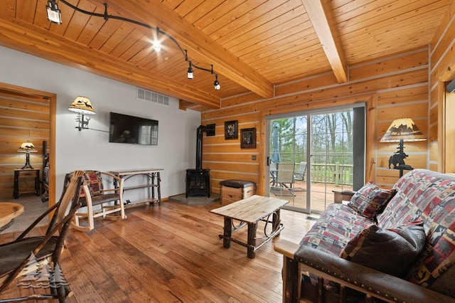 living area with wood-type flooring, beam ceiling, wood ceiling, and a wood stove