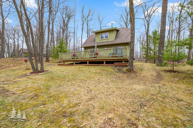 back of house with roof with shingles, a lawn, and a deck