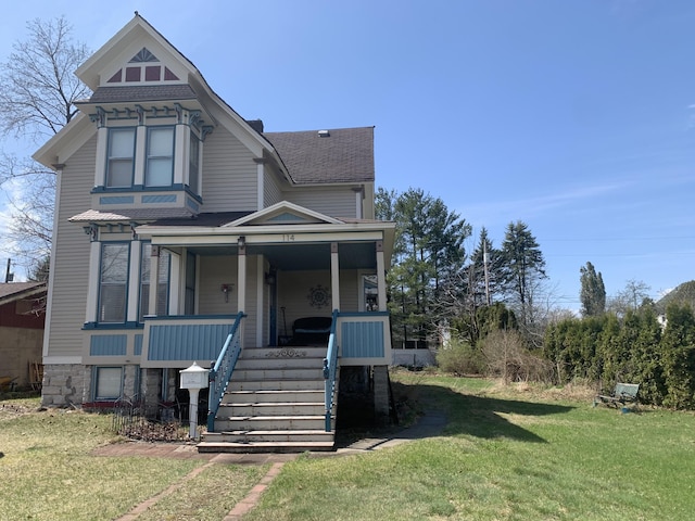 victorian house with covered porch, a shingled roof, a front lawn, and stairway