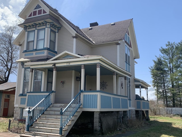 victorian home with a porch, a shingled roof, stairs, and a chimney
