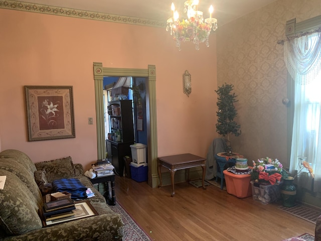 living room featuring an inviting chandelier, wallpapered walls, and wood finished floors