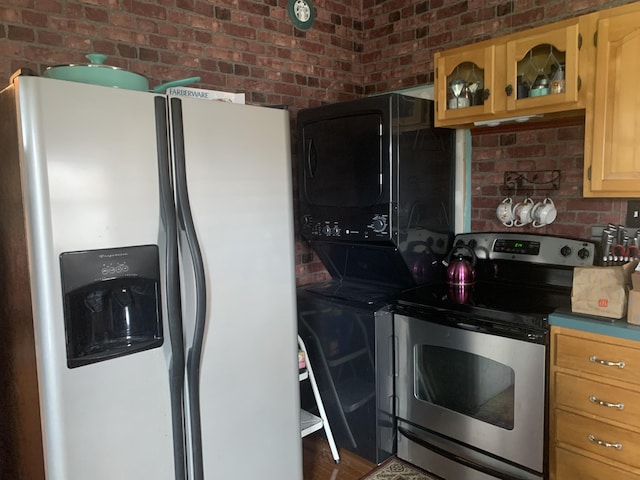 kitchen featuring stainless steel appliances, brick wall, glass insert cabinets, and stacked washer and clothes dryer
