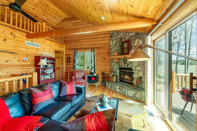 living room featuring lofted ceiling with beams, wood-type flooring, a stone fireplace, visible vents, and wood ceiling