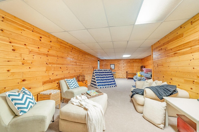 carpeted living area with wood walls and a drop ceiling