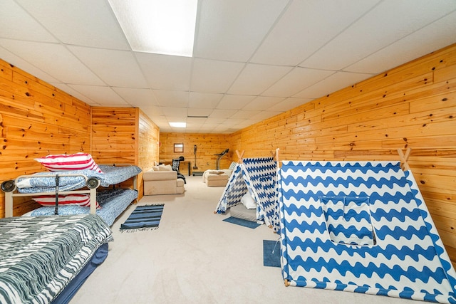 carpeted bedroom featuring wooden walls and a drop ceiling