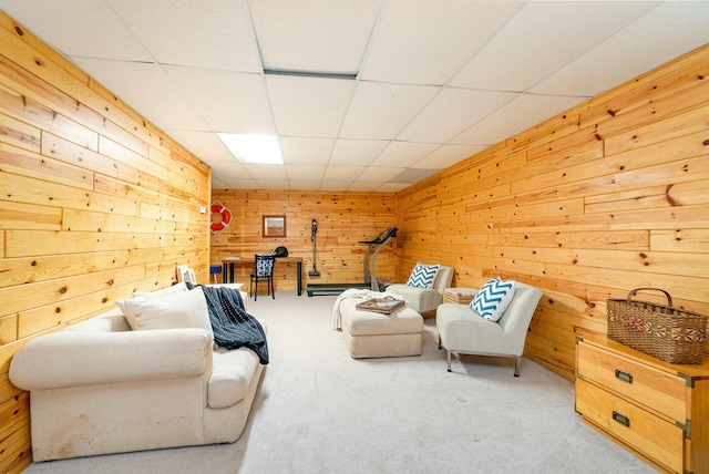 carpeted living area with wood walls and a drop ceiling