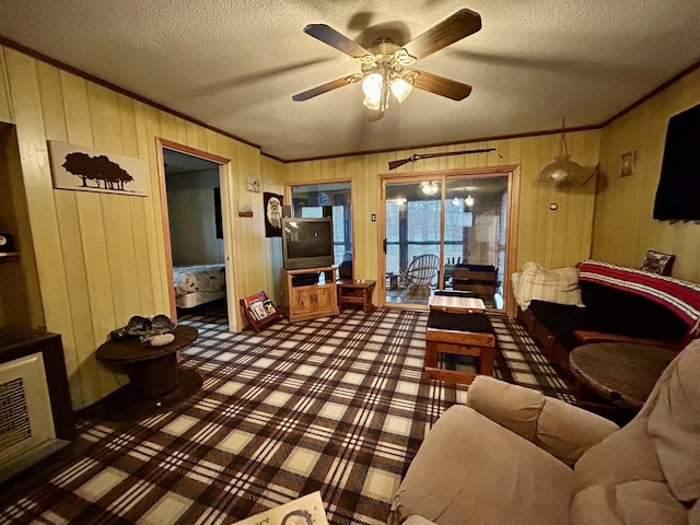 carpeted living area featuring wooden walls, a ceiling fan, a textured ceiling, and ornamental molding