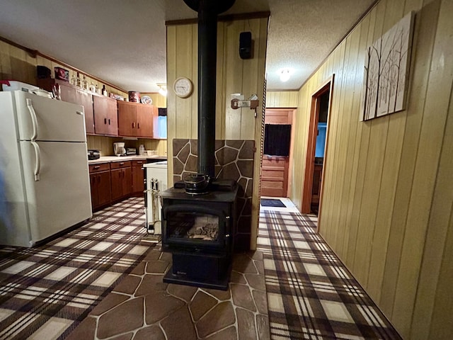 kitchen with a wood stove, light countertops, a textured ceiling, wood walls, and freestanding refrigerator
