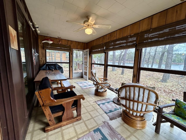sunroom / solarium featuring a ceiling fan, tile patterned floors, and wood walls