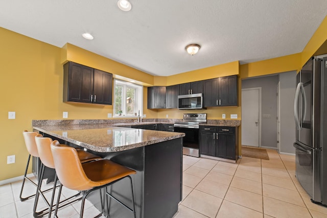 1406 Opal Lake Rd, Gaylord, MI 49735 - kitchen with stainless steel appliances, a peninsula, a breakfast bar area, light stone counters, and baseboards