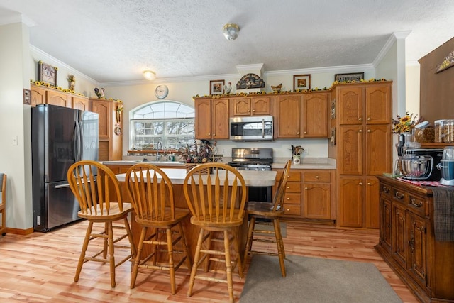 6075 W Edgar St, Pellston, MI 49769 - kitchen featuring appliances with stainless steel finishes, a textured ceiling, brown cabinetry, light wood-type flooring, and a center island