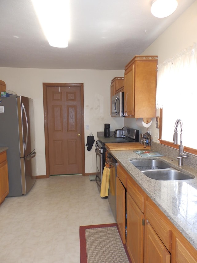kitchen featuring a sink, stainless steel appliances, brown cabinets, light floors, and light stone countertops