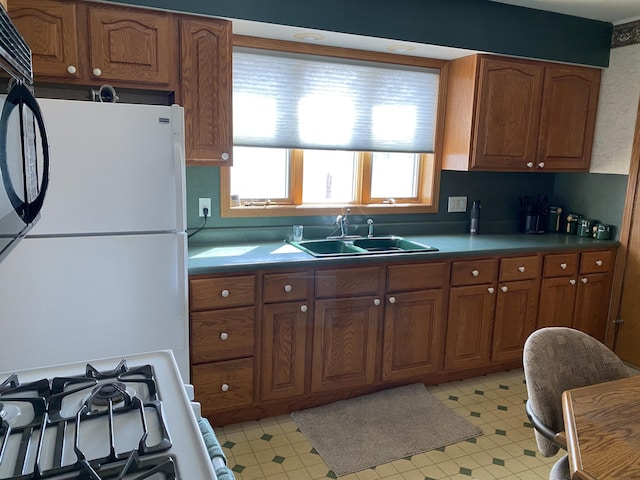 kitchen featuring a sink, freestanding refrigerator, stove, and brown cabinets