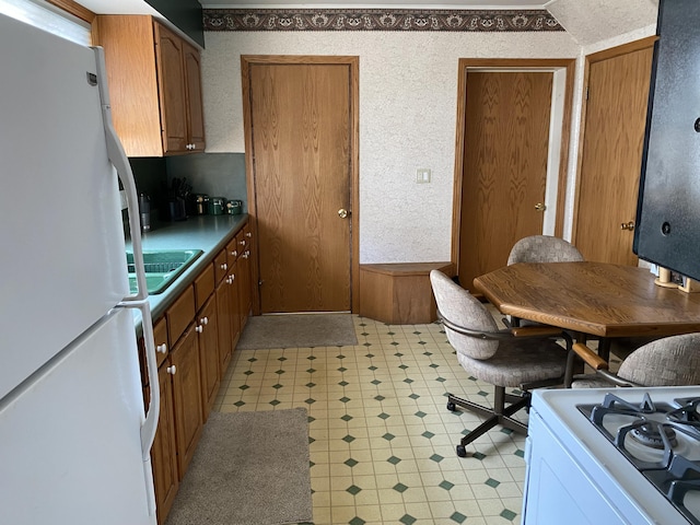 kitchen with a sink, light floors, brown cabinets, and white appliances