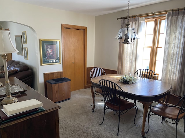 dining space with arched walkways, a wainscoted wall, and light colored carpet