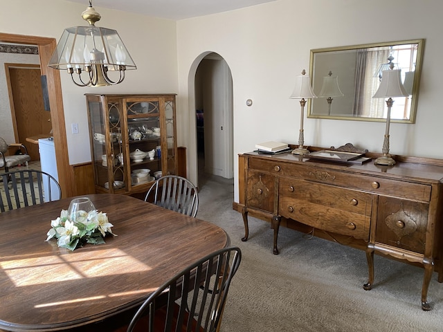 dining space featuring arched walkways, carpet flooring, and a chandelier