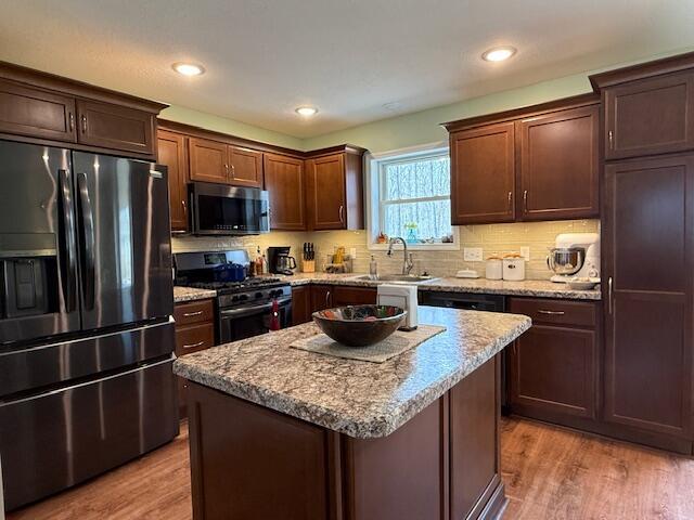 kitchen with a sink, appliances with stainless steel finishes, light wood finished floors, and light stone counters